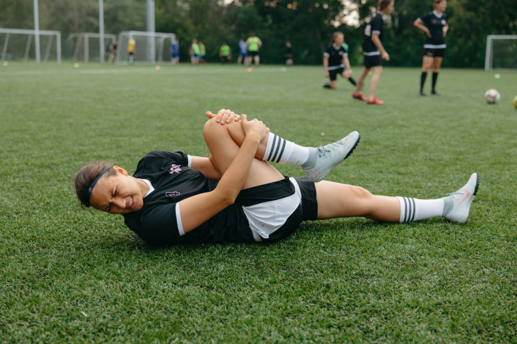 player injured in sports match lying on the ground holding her leg.