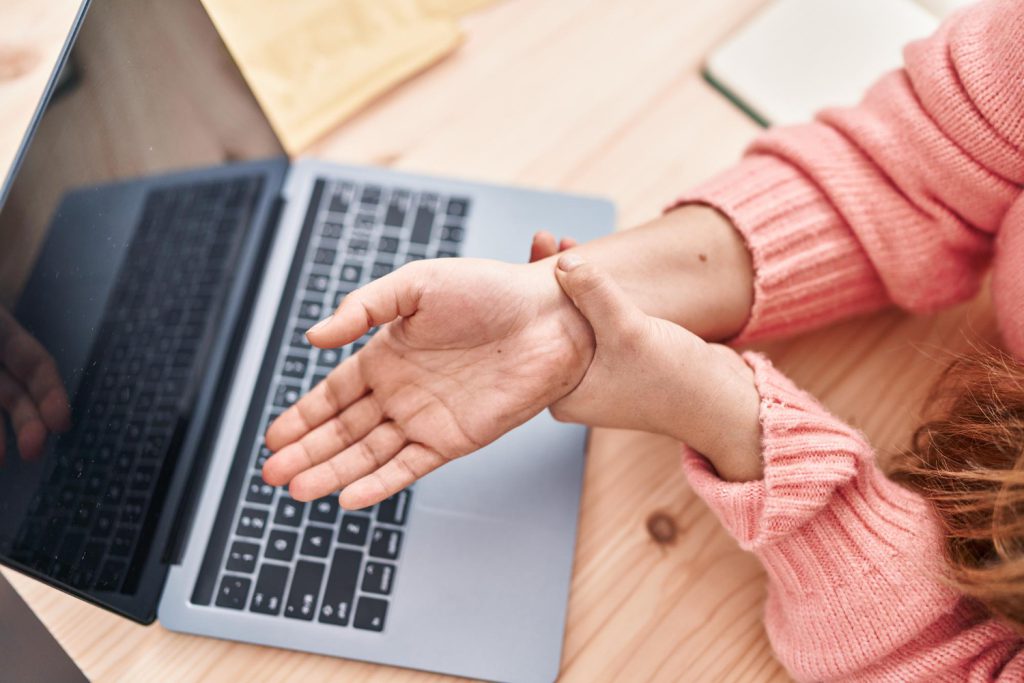 Woman holding her painful wrist at a laptop